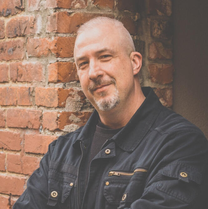 Chris Powell leaning against a brick building wall